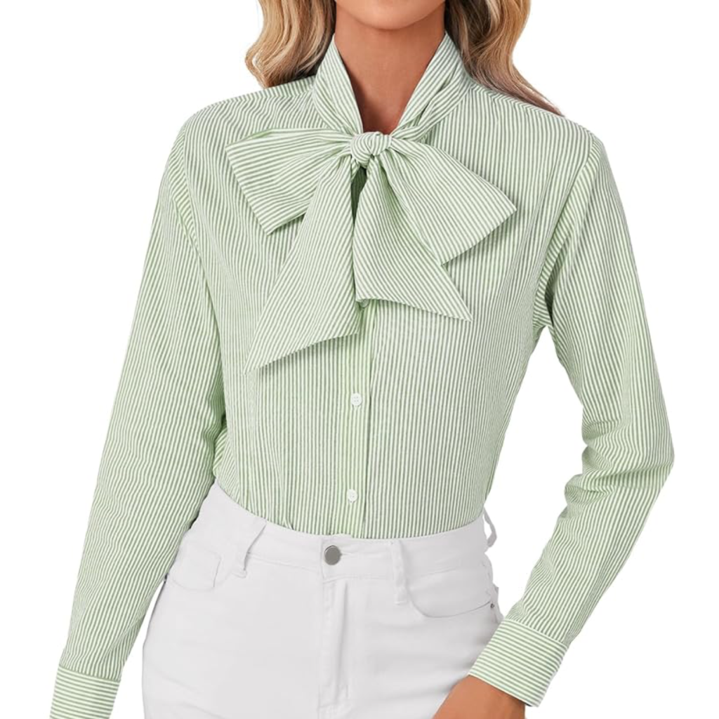 A woman wearing a soft sage green silk bow tie blouse with a large elegant bow, tucked into white trousers for a fresh and professional spring look.