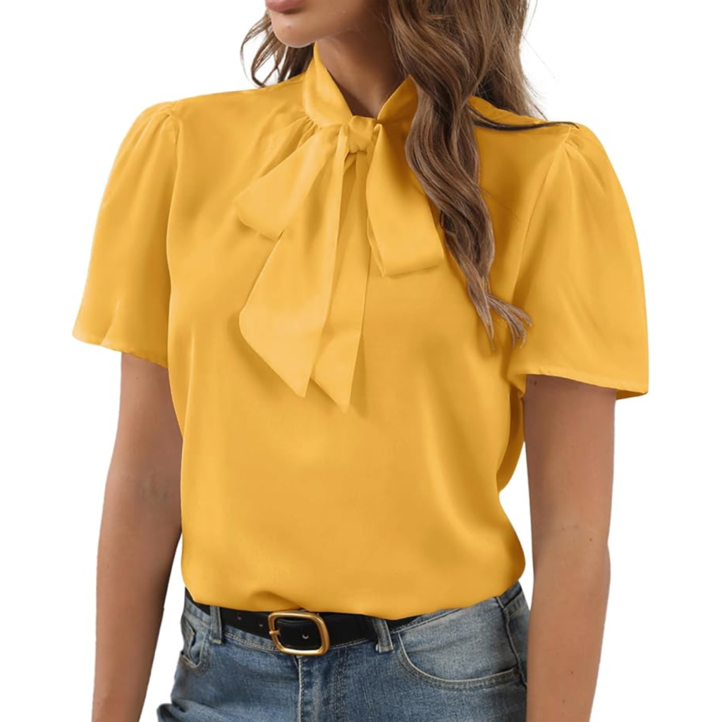 A woman wearing a mustard yellow short-sleeve bow tie blouse with a high-neck pussy-bow, tucked into blue jeans for a chic and colorful casual-professional look.