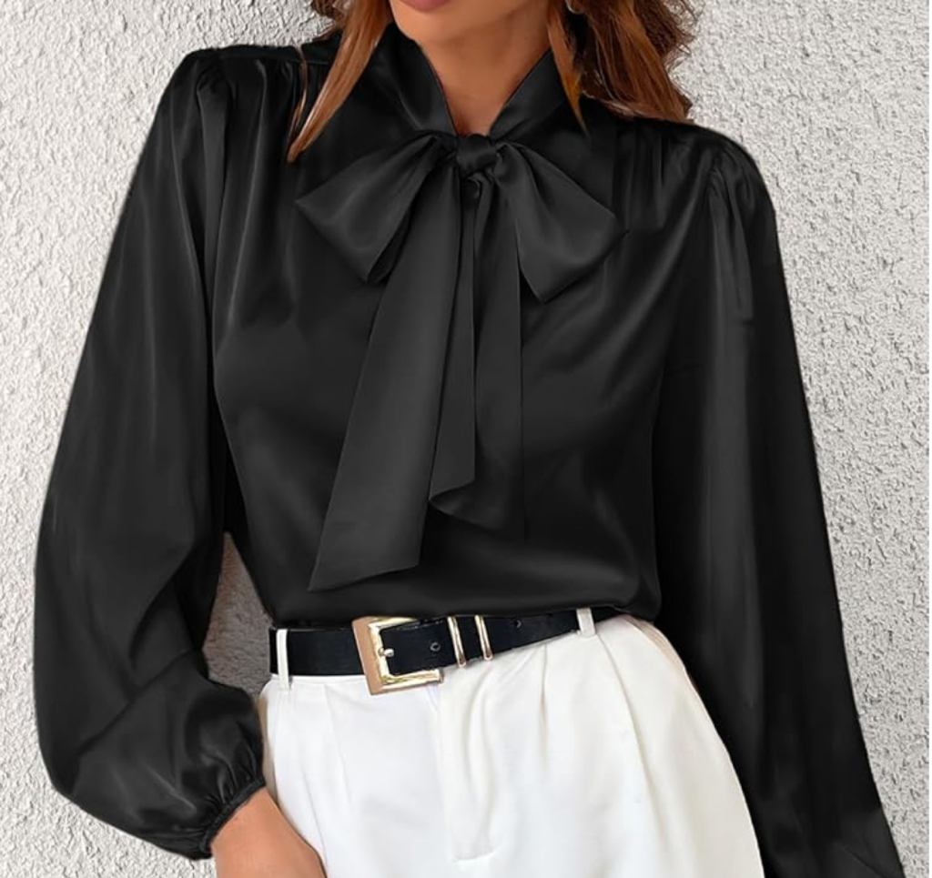 A woman wearing an elegant black silk bow tie blouse and dark sunglasses, portraying a sophisticated and timeless "pussy-bow" fashion style in an urban setting.