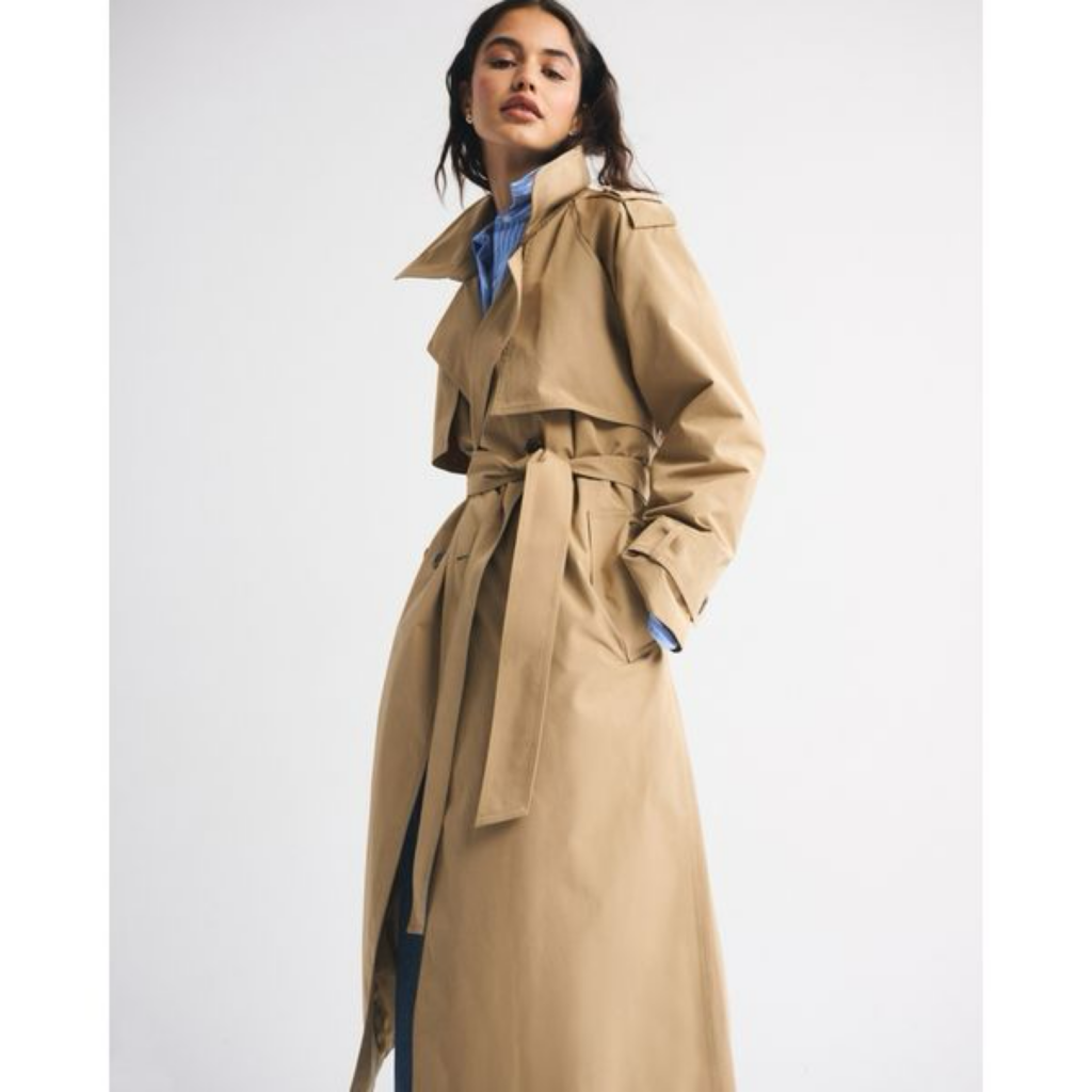 A classic beige double-breasted trench coat with a belted waist and structured collar, featured on The Posh EdiT as a spring capsule wardrobe staple.