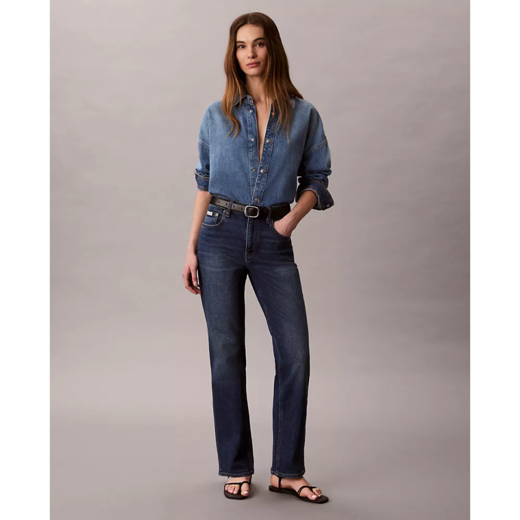 A model wearing Calvin Klein High Rise Straight Jeans in a dark vintage wash, styled with a matching denim button-down shirt and black sandals for a minimalist 90s aesthetic.