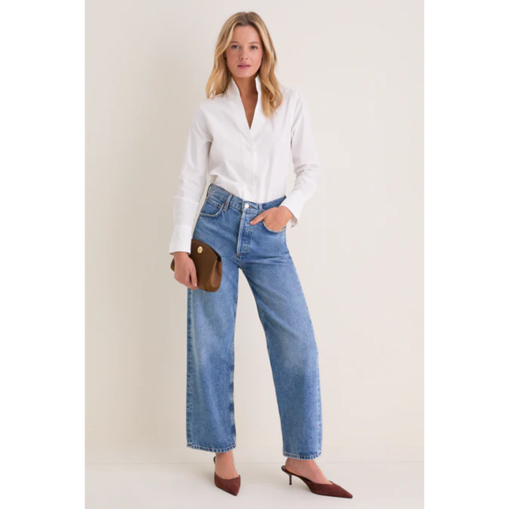 A model wearing the Tuckernuck White Bessette Button Down shirt in crisp white cotton, tucked into wide-leg blue jeans and styled with a brown clutch for a classic 90s minimalist look.