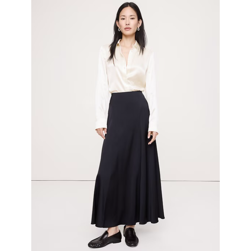 A model wearing the Banana Republic Everyday Silk Shirt in off-white, paired with a high-waisted black maxi skirt and black loafers for a sophisticated 90s minimalist ensemble.